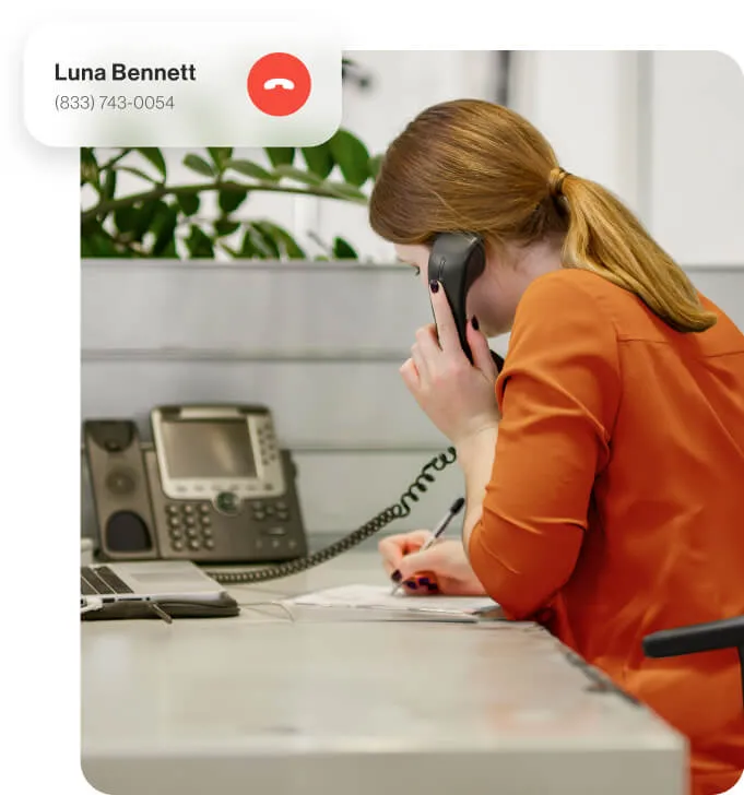A female employee using a VoIP desk phone to take a phone call