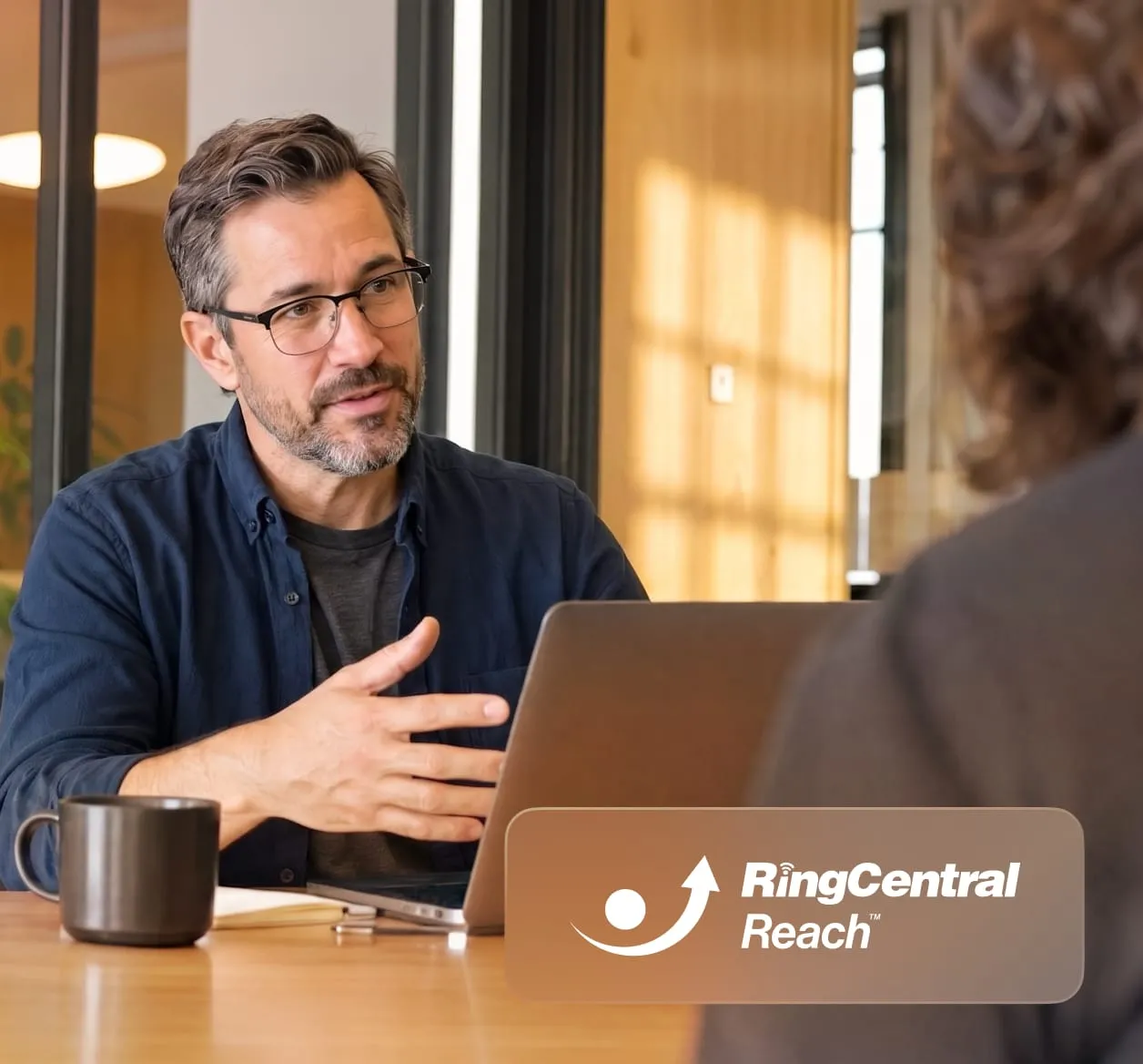 A man in glasses explaining to a woman across the table with inlay of RingCentral Reach logo