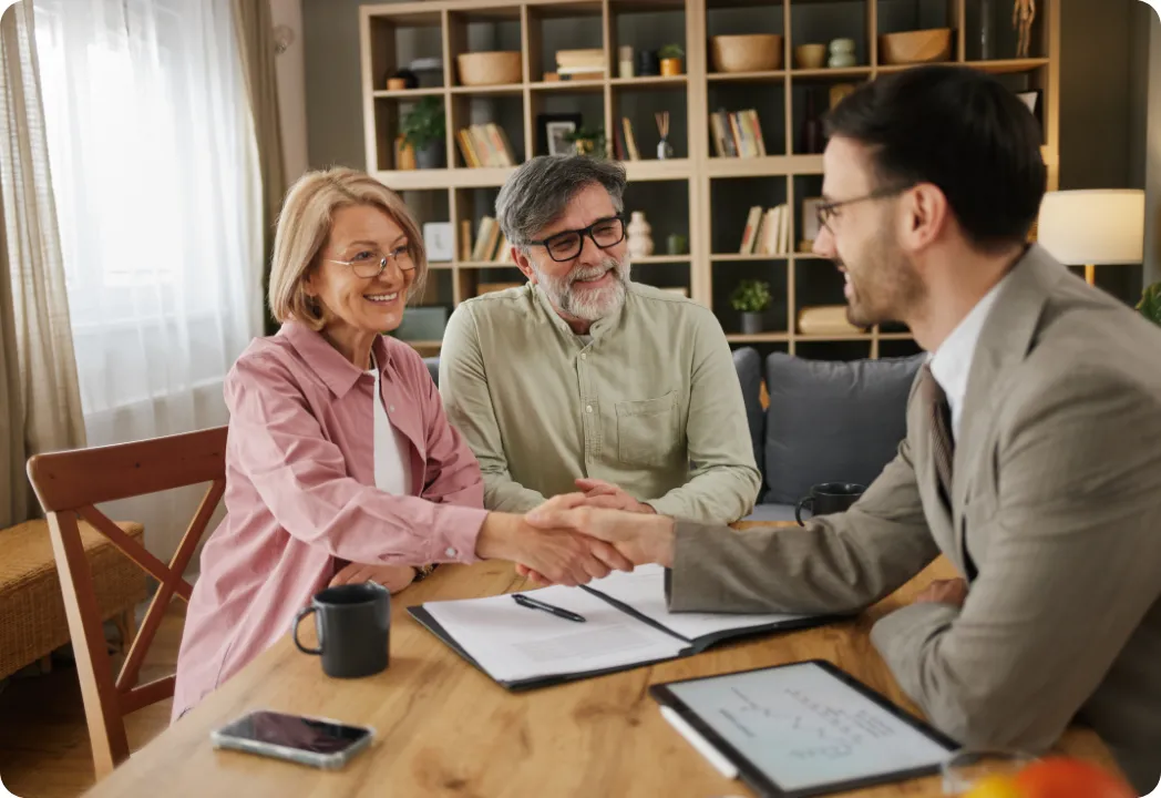 A couple shakes hands with an insurance agent, symbolizing a successful property transaction.