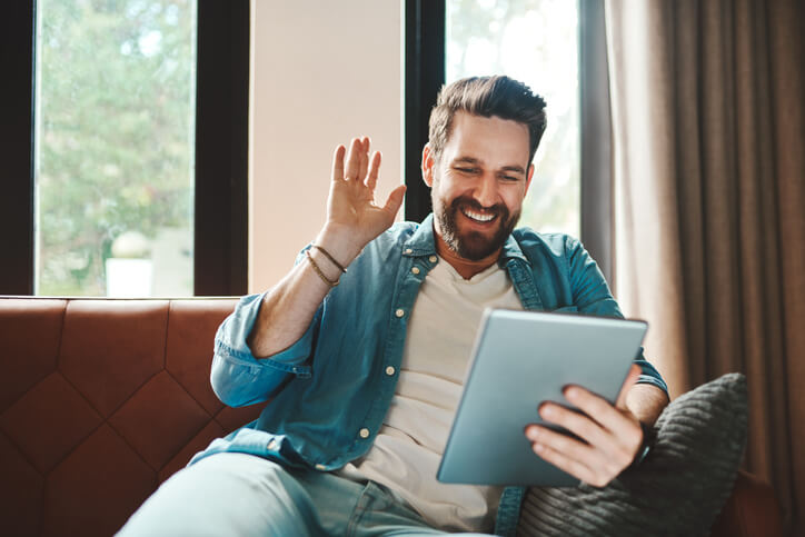 Remote worker on a video call using his tablet while chilling on the sofa at home